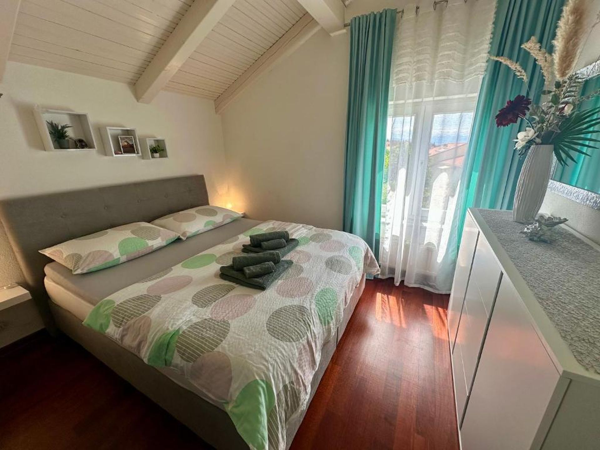 Une chambre à coucher avec un lit, une table de chevet, une fenêtre avec des rideaux et un mur orné de trois tableaux.