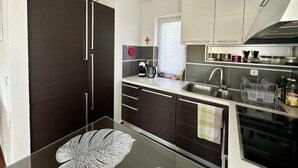 Eine moderne Küche mit dunklen Schränken, einem Glastisch und einem Fenster mit Jalousien.