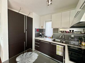 Eine moderne Küche mit dunklen Schränken, einem Glastisch und einem Fenster mit Jalousien.