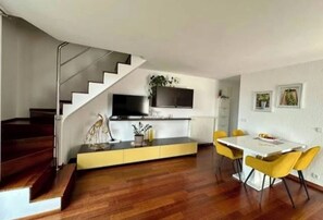 A modern living space with a staircase, a dining area with yellow chairs, a kitchen with a TV, and a plant on the counter. - Apartment Kinaya (Crikvenica)