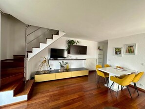 Eine moderne Küche mit eingebautem Ofen und Mikrowelle, ein Essbereich mit gelben Stühlen und eine Treppe, die zu einer weiteren Ebene führt.
