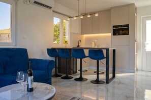Eine moderne Küche mit Barhocker, einem Esstisch mit Weingläsern und einem blauen Sofa.