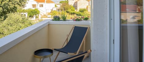 A balcony with two chairs and a small table, overlooking a residential area with houses and greenery.