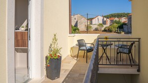 Uma varanda com mesa e cadeiras, um vaso de planta e vista para casas ao fundo.