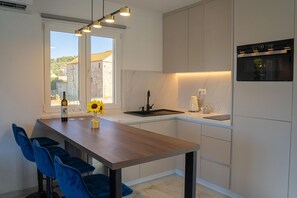 Uma cozinha moderna com mesa de madeira, cadeiras azuis, forno embutido e janela com vista para edifícios.