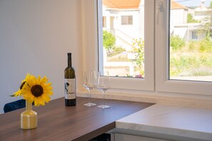 Ein Tisch mit einer Weinflasche und zwei Gläsern, eine Vase mit einem Sonnenblume und Blick auf Häuser durch ein Fenster.