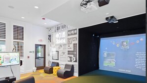 Un'area lounge moderna con un grande schermo per presentazioni, sedute confortevoli e un proiettore.