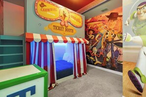 A room with a ticket booth, a bed with striped curtains, and a mural with animated characters. - Disney Villa | Theater, Pool & Game Room Sleeps 22 (Kissimmee)
