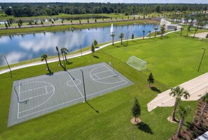 An outdoor basketball court with a water body and trees in the background. - Disney Villa | Theater, Pool & Game Room Sleeps 22 (Kissimmee)