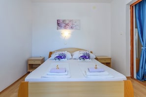 Ein Schlafzimmer mit einem Bett, zwei Kissen, einem Nachttisch, einer Wandleuchte und einem Fenster mit Vorhängen.