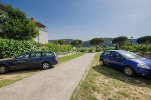 Two parked cars on a gravel path with a building and greenery on one side and a hilly landscape in the distance. - Rooms Borka (Lopar)