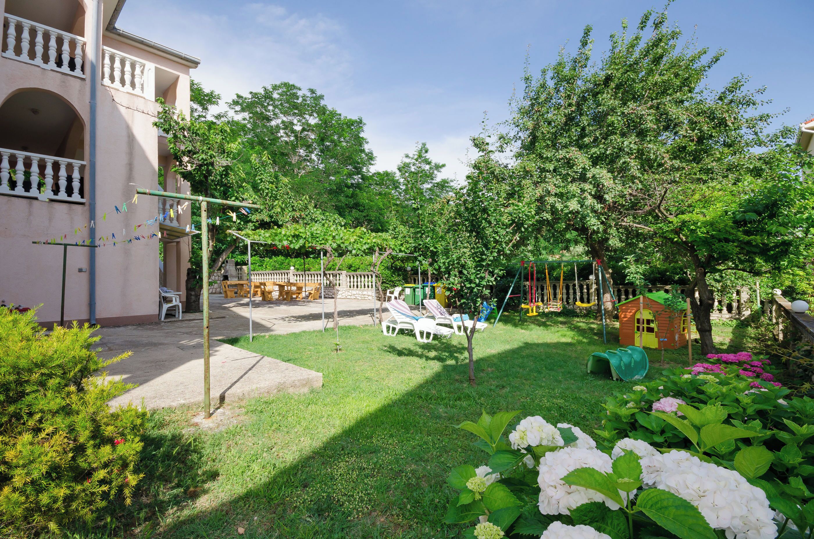 Ein Innenhof mit Sitzgelegenheit, einer Spielanlage und einem kleinen Garten mit Hortensien.