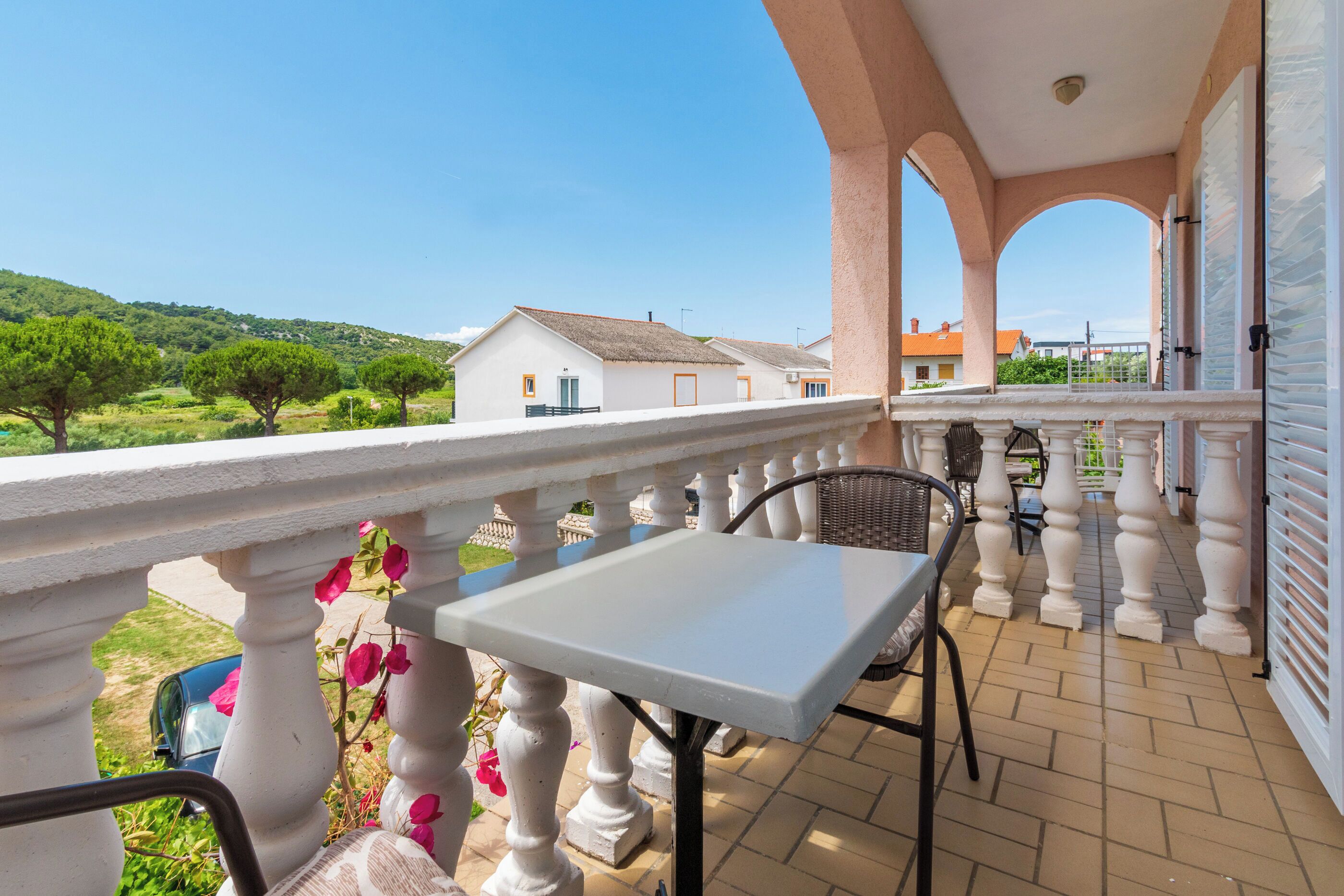 Ein Balkon mit Tisch und Stühlen, der auf einen Wohnbereich mit Häusern und Grünblicken blickt.