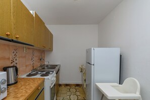 A compact kitchen with wooden cabinets, a gas stove, a sink, and a white refrigerator. - Rooms Borka (Lopar)