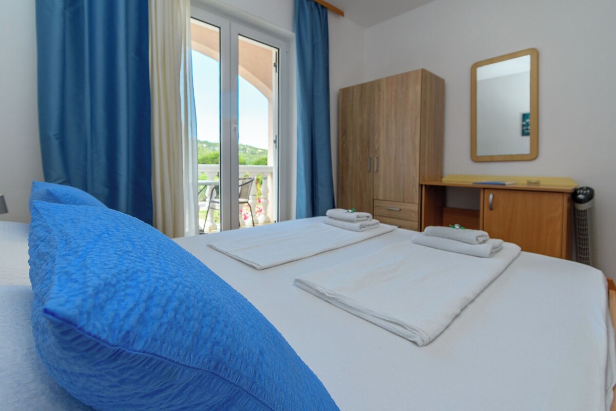 A hotel room with a bed, a wooden wardrobe, a mirror, and a view of the outdoors.