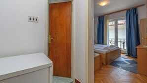 Ett hotellrum med en dörr av trä, ett litet skrivbord, en säng och utsikt över omgivningen genom ett fönster med blå gardiner.