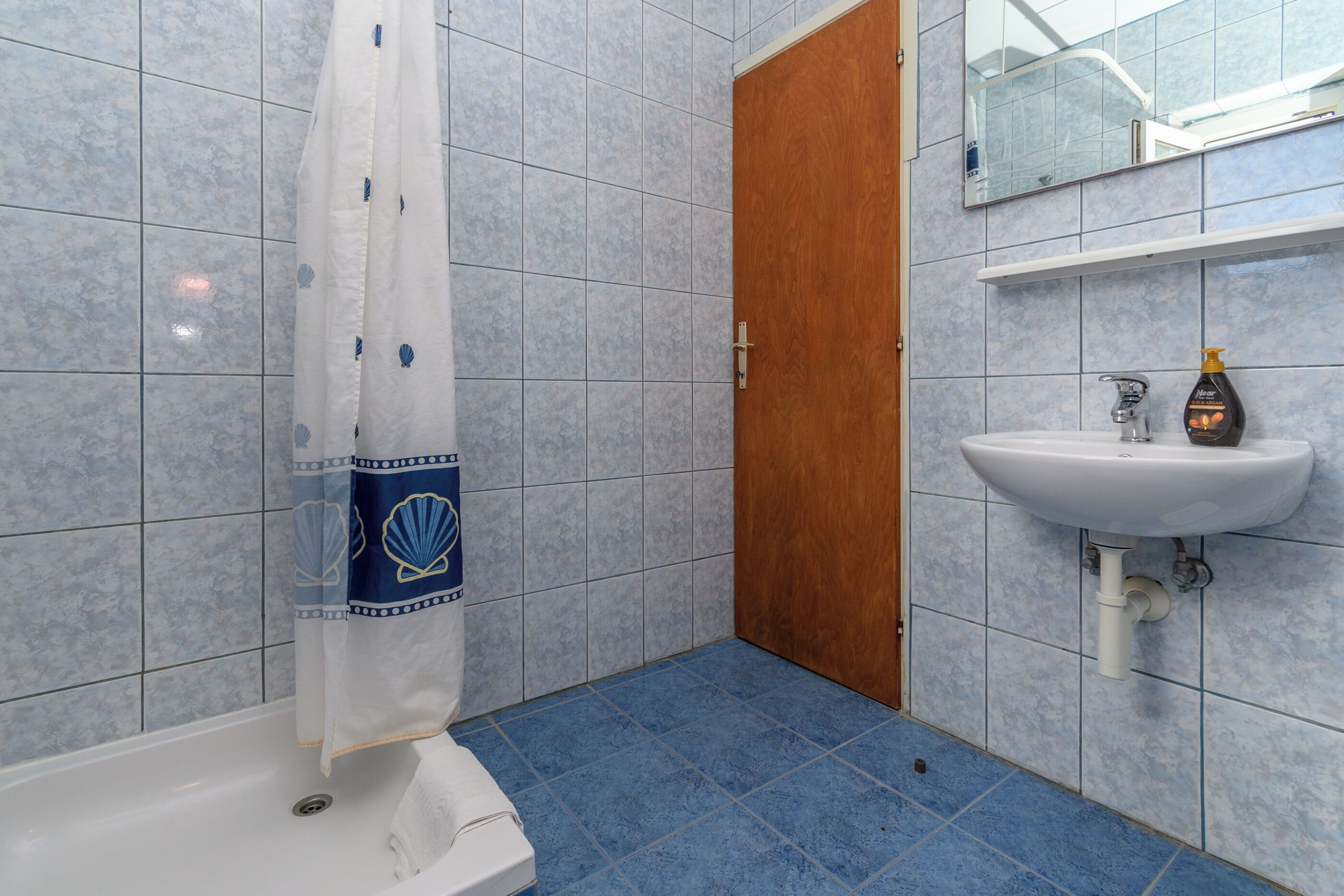 A bathroom with a shower, a sink, and a wooden door.