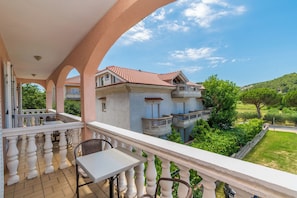 Ein Balkon mit Tisch und Stühlen, der auf ein Gebäude mit rotem Ziegeldach und eine üppige, grüne Landschaft blickt.