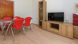 A room with a dining table, red chairs, a wooden cabinet with a TV, and a wooden door.