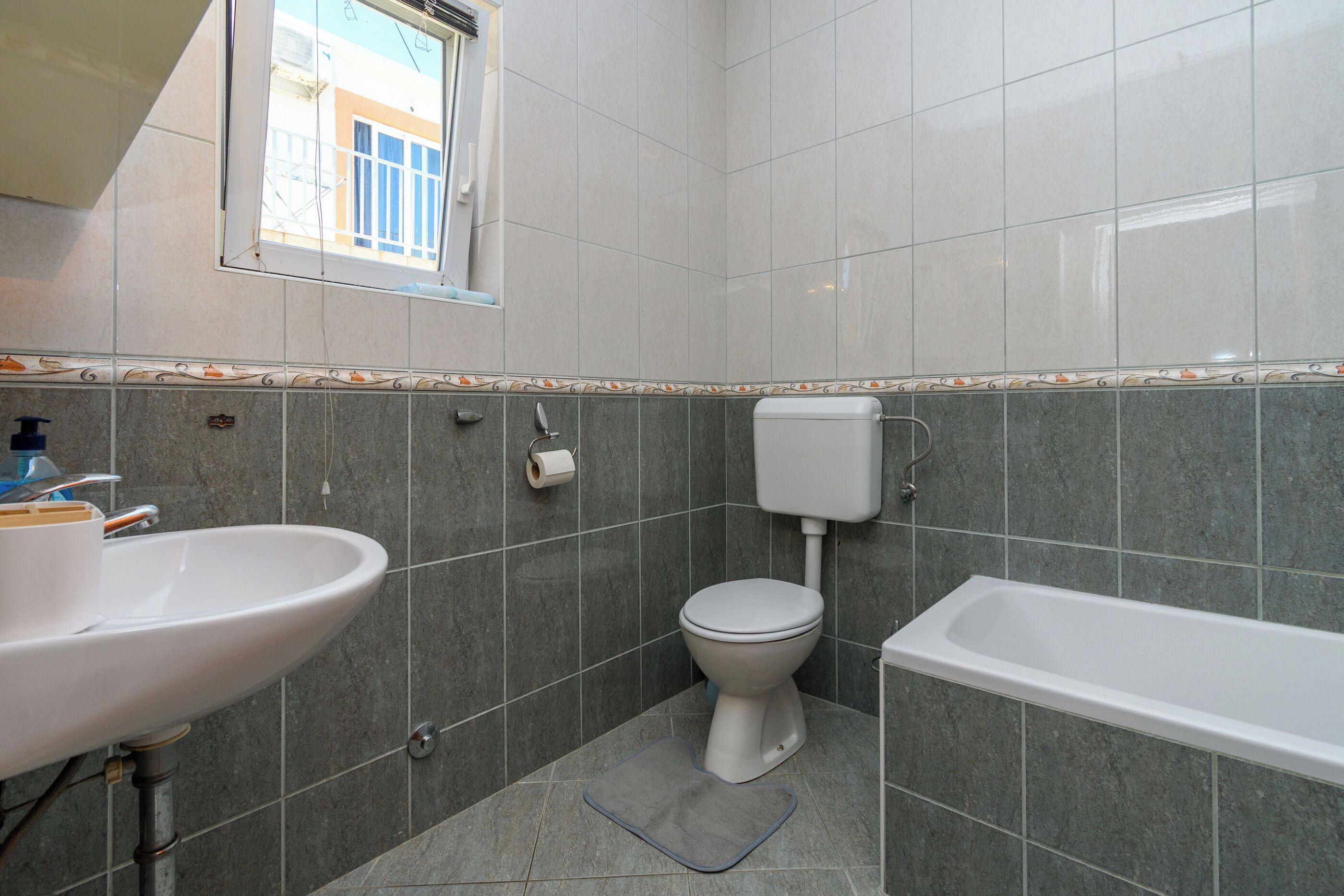 A bathroom with a sink, toilet, and bathtub, tiled in a uniform pattern.