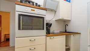 A compact kitchen with a built-in oven, a microwave, and a sink. There are cabinets with handles and a trash bin.