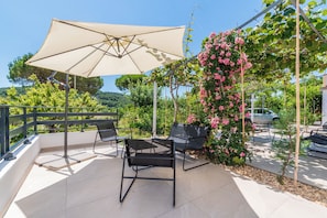 Une terrasse extérieure avec une table et des chaises, un grand parasol et une tonnelle recouverte de fleurs.