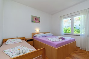 Une chambre avec deux lits, une table de chevet, une lampe fixée au mur et une fenêtre avec des rideaux.