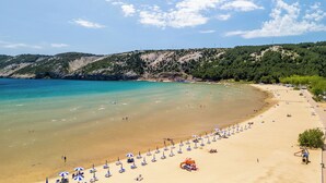 A beach with clear turquoise water, sandy shore, and a hilly backdrop.