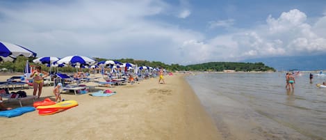 A beach with umbrellas, lounge chairs, and people.