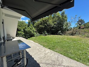 Ein Patio mit Tisch und Stühlen, einem Betonboden und einem Rasen mit Bäumen im Hintergrund.