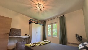 Un dormitorio con cama, armario, escritorio con silla, ventana con cortinas e iluminación en el techo.