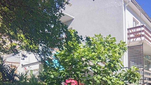 Un edificio residencial con muro de piedra, follaje y cielo azul despejado.