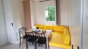 Um espaço de estar compacto com mesa e cadeiras, um sofá amarelo e uma janela com vista para o verde.