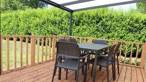 Um alpendre coberto com um deck de madeira, uma mesa e quatro cadeiras.