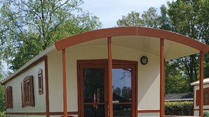 A small, single-story cabin with a covered porch, a table, and a bench. - Verblijf in een unieke Pipowagen | De Otterberg (Wijster)