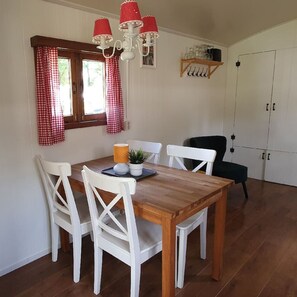 A dining area with a wooden table, white chairs, a red and white checkered window, and a chandelier.