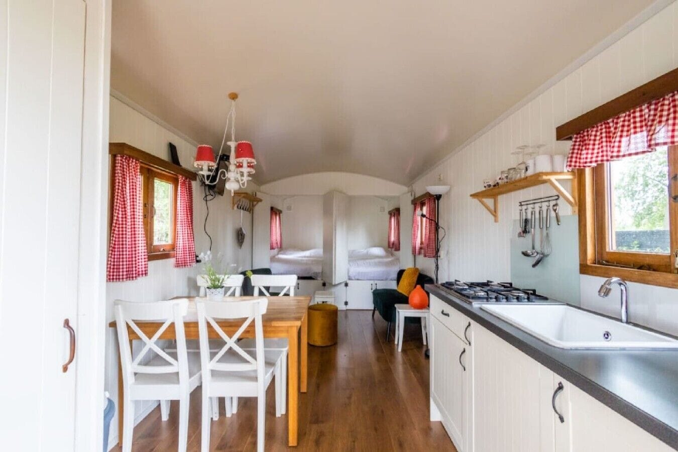 Une cuisine de taille réduite avec des meubles blancs, une table à manger en bois et une fenêtre ornée de rideaux à carreaux.