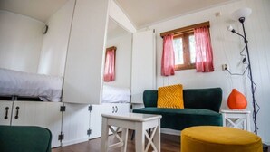 A room with a bunk bed, a green sofa, a small white table, and a yellow ottoman. - Verblijf in een unieke Pipowagen | De Otterberg (Wijster)