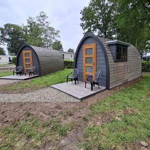 Two small, semi-circular cabins with wooden doors and windows, each with a set of chairs outside.