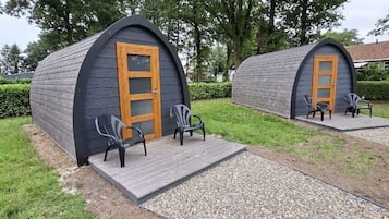 Two small, dark-colored cabins with wooden doors and black chairs outside.