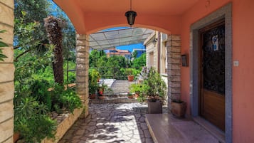 Un paseo techado con suelo de piedra, macetas con plantas y vistas a una zona residencial.