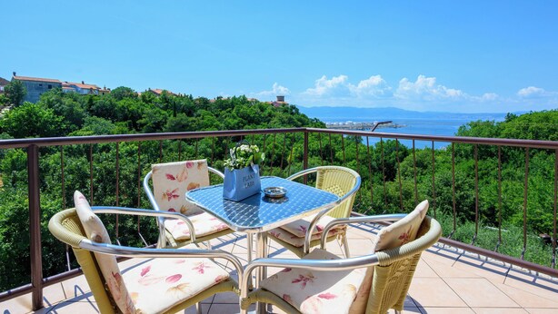 A balcony with a table and chairs, overlooking a coastal landscape with buildings and greenery. - Room Marta (Omisalj)
