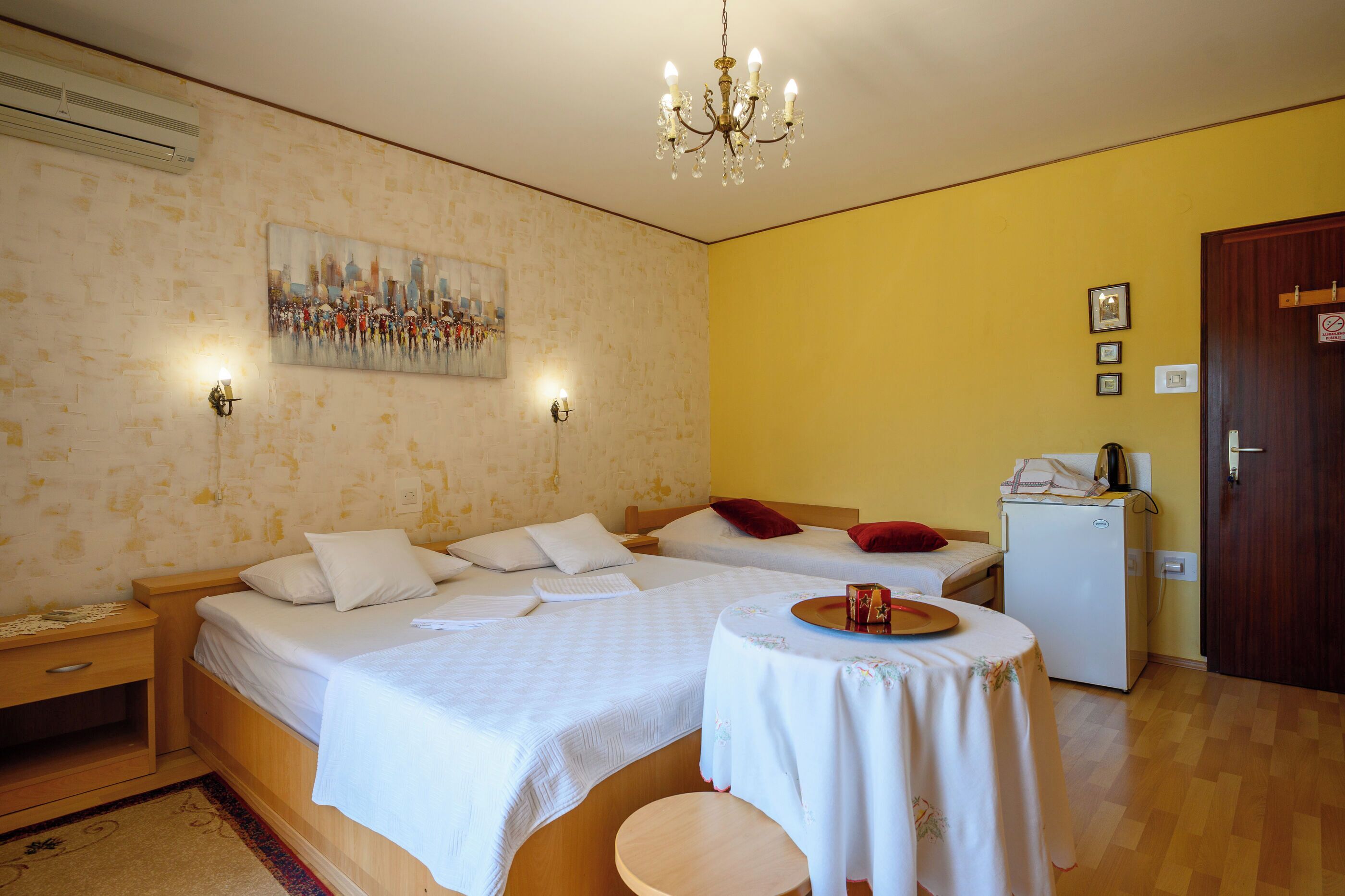 A hotel room with two beds, a small table, a refrigerator, and a painting on the wall.