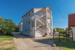 A two-story building with a staircase, a balcony, and a paved entrance area. - Apartments Mande (Rab)