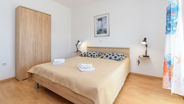 A bedroom with a bed, a wardrobe, a painting, and two bedside lamps. - Apartments Mande (Rab)