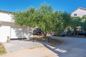 A residential area with a tree in front of a house, a garage, and parked cars. - Apartments Mande (Rab)