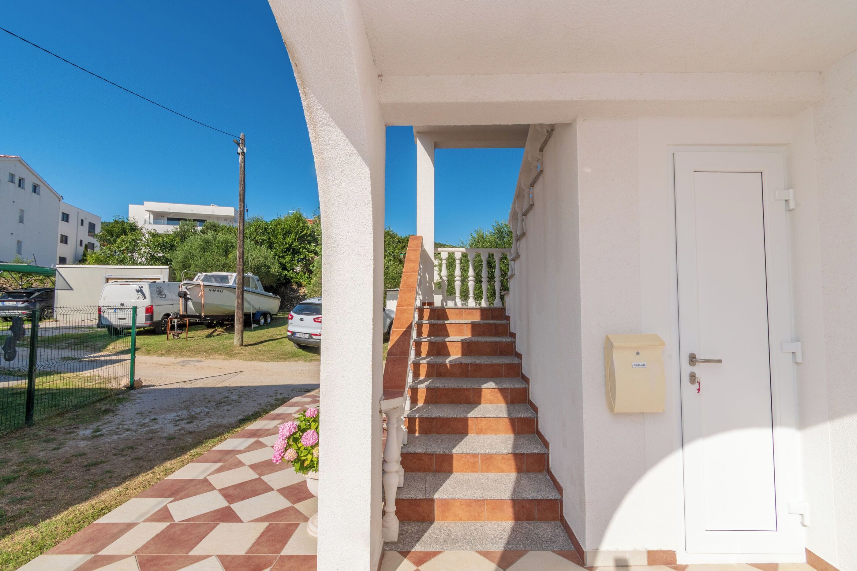 A staircase leading to a white door, a checkered tile floor, and a vehicle parked outside.
