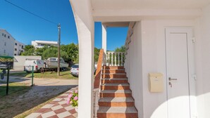 A staircase leading to a white door, a checkered tile floor, and a vehicle parked outside. - Apartments Mande (Rab)