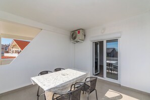 Ein Balkon mit Tisch und Stühlen, einer Klimaanlage und einer Glasschiebetür zu einem Außenbereich.