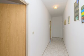 A hallway with a wooden door, white walls, and tiled flooring. - Apartments Mande (Rab)